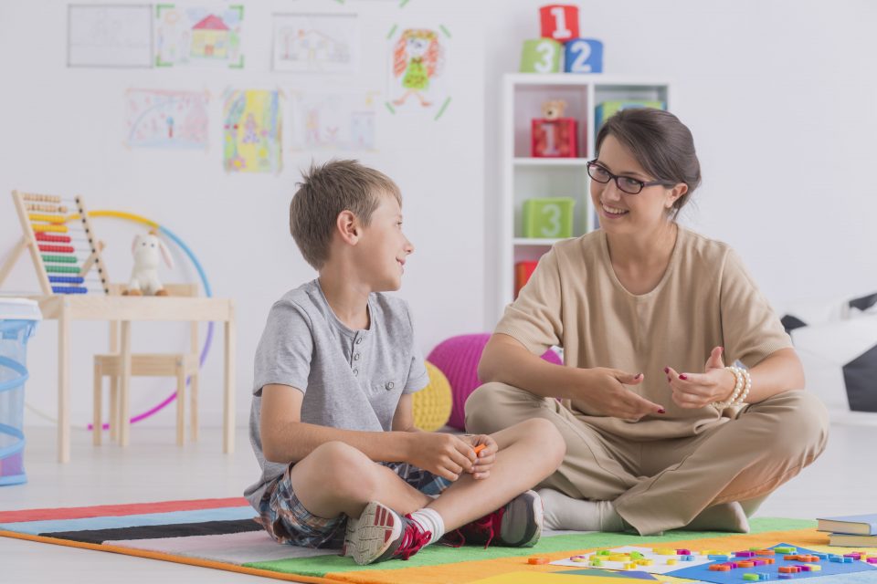 Smiling young boy and therapist sitting on floor and talking at home