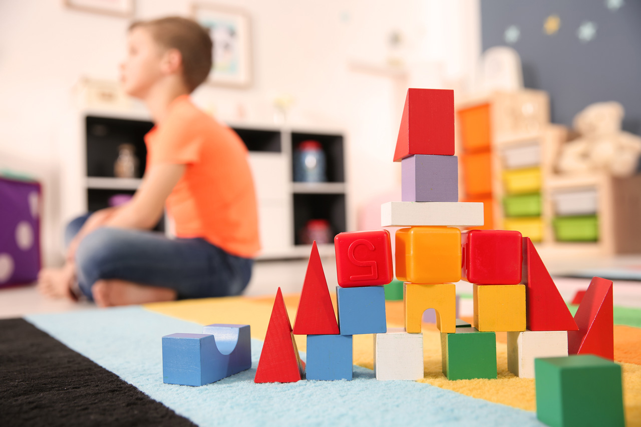 Colorful plastic and wooden blocks sitting on a blue and yellow rug with young child in the background