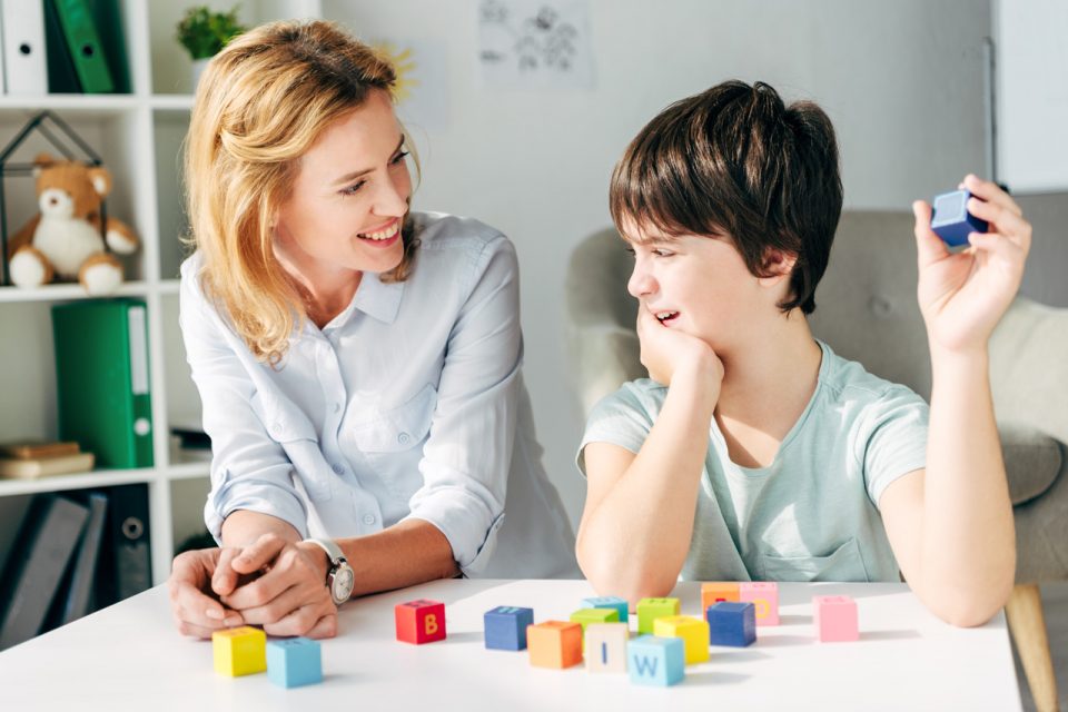 Young boy with brown hair holding a blue block smiles during therapy session