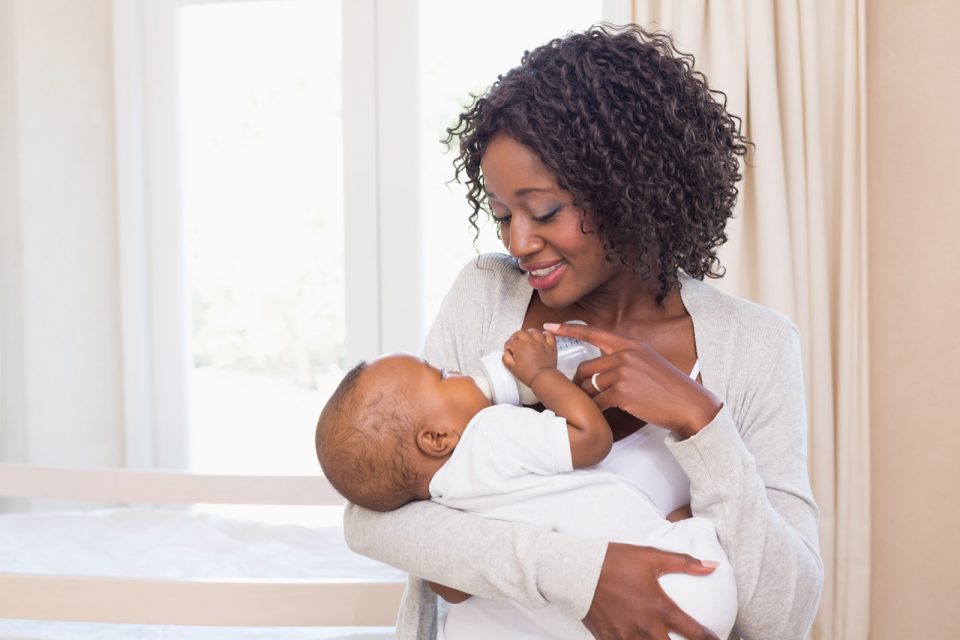 African American mom wearing soft tan sweater feeding her baby a bottle of milk