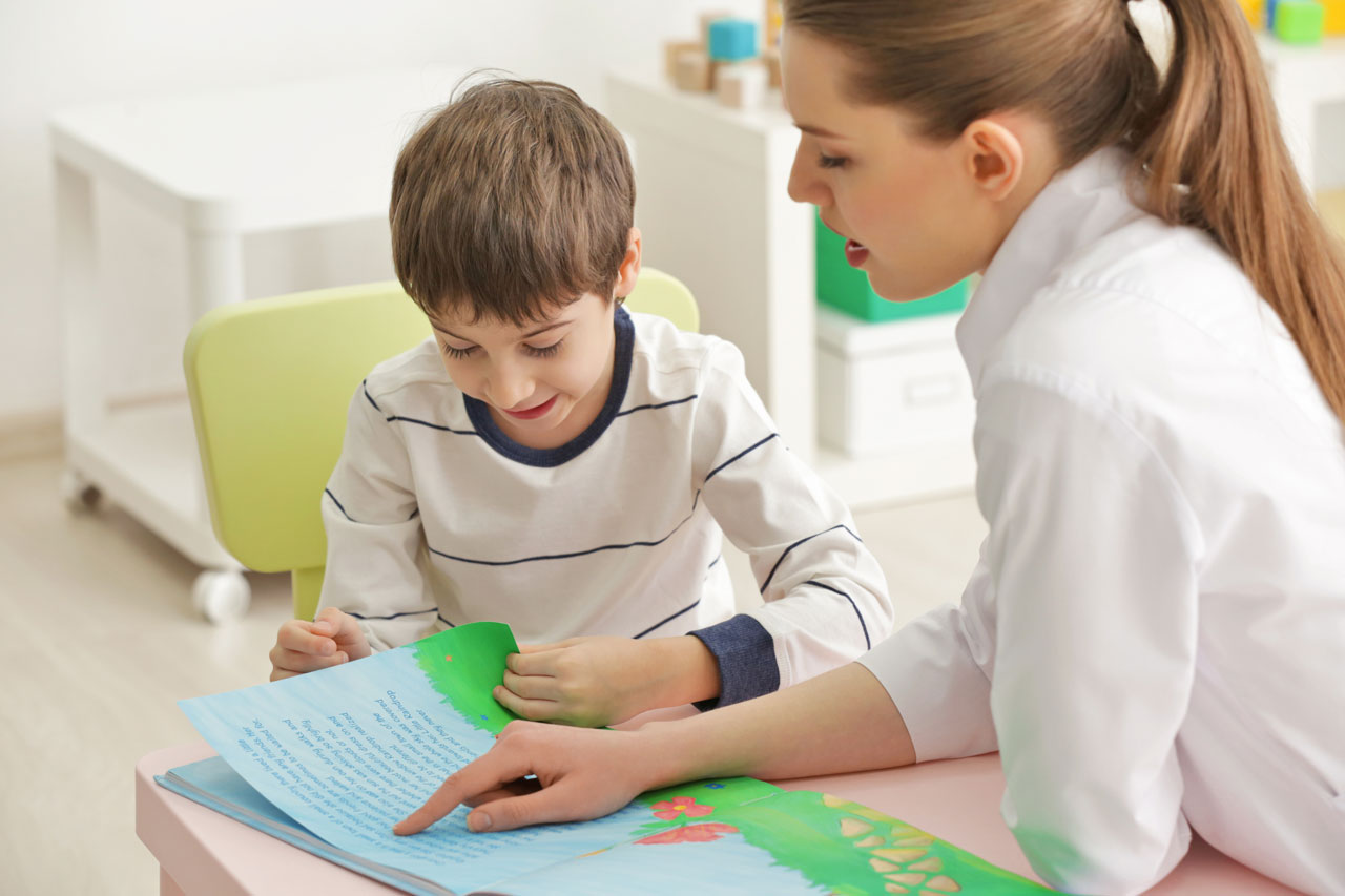 little boy reads book while clinician assesses