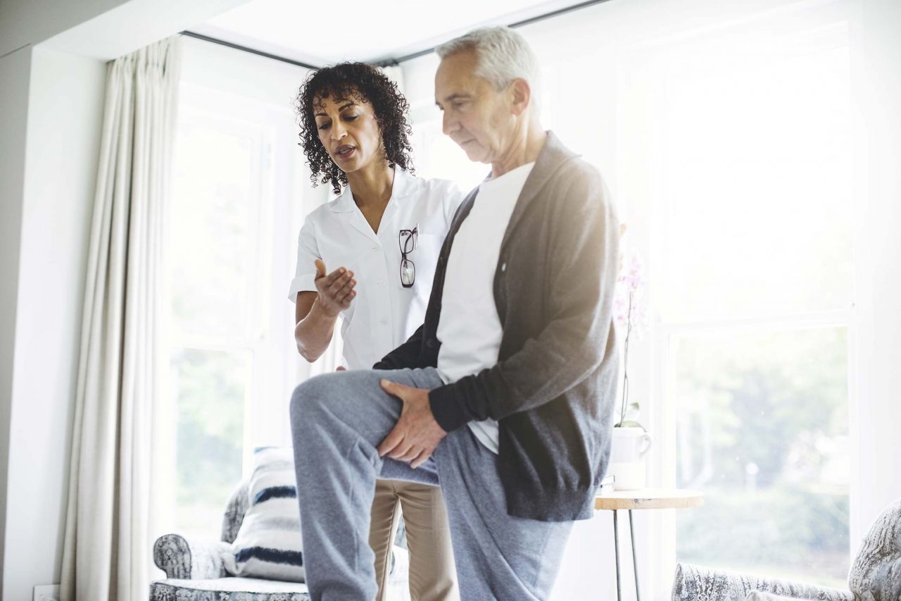 older male working on lifting leg for physical therapy at home with help from physical therapist