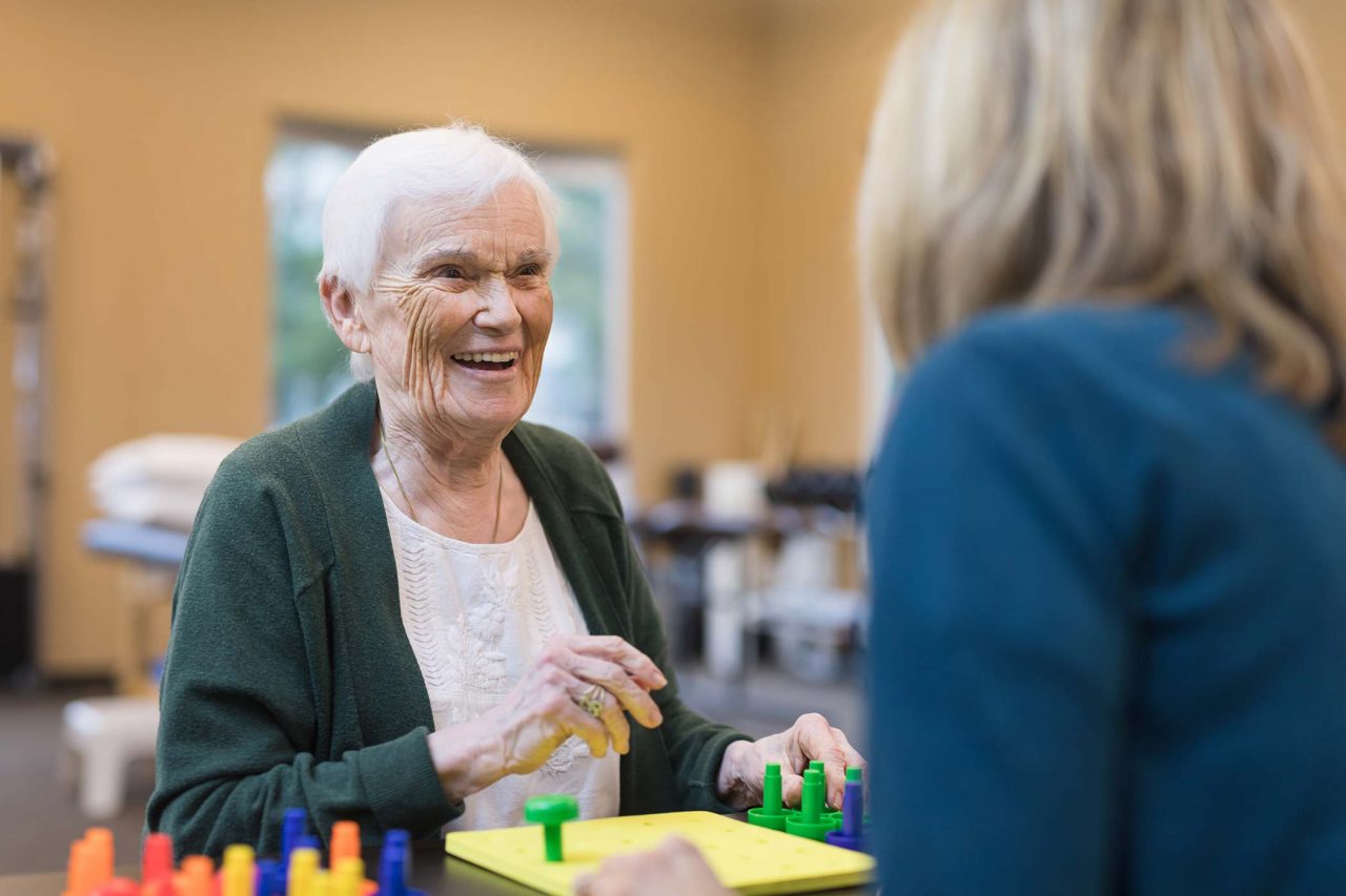 Occupational therapist works with smiling senior woman in green cardigan and white floral embroidered shirt