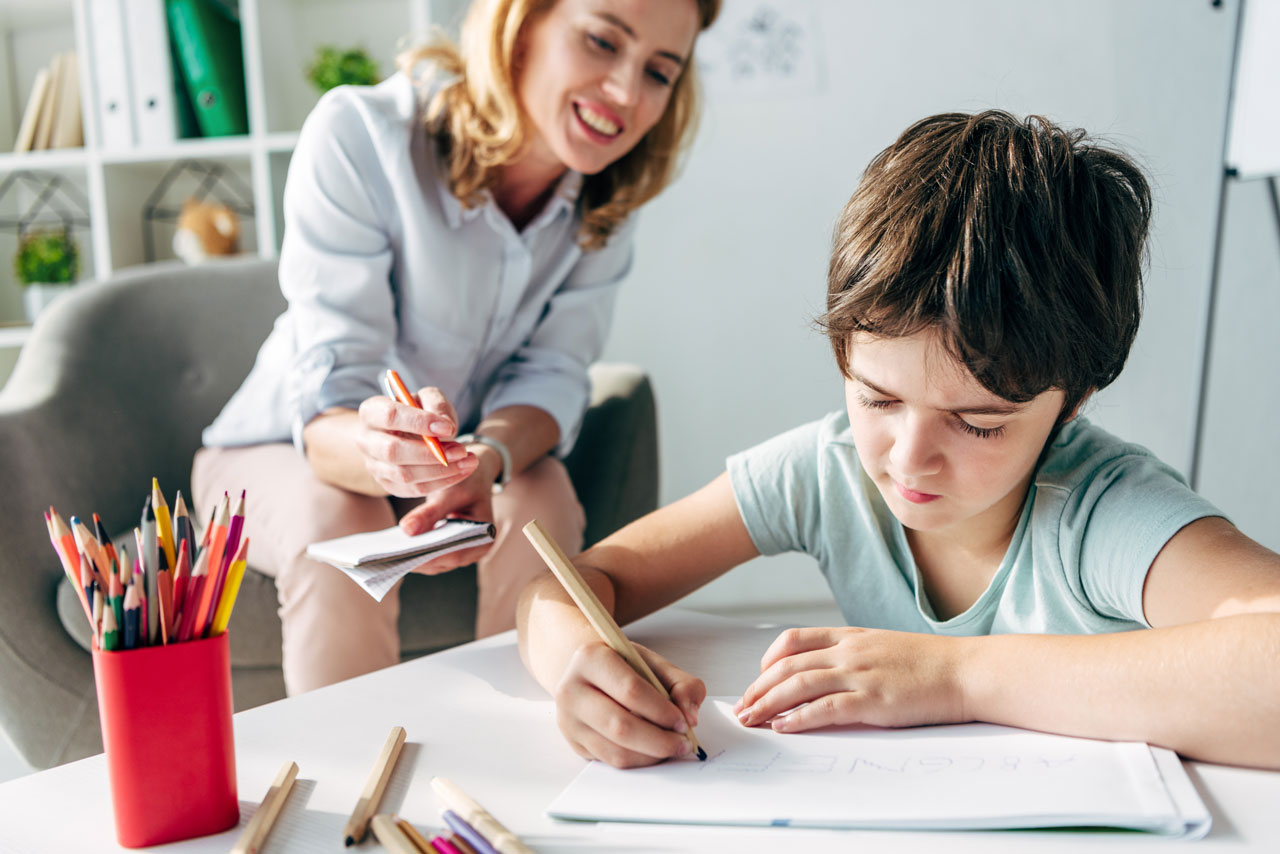 kid drawing on paper with pencil and clinician assessing